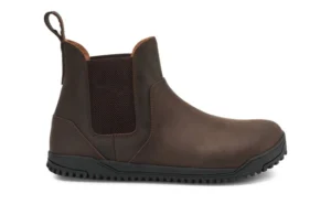 A brown leather Chelsea Boot by Xero Shoes with a black rubber sole, elastic side panel, pull tab at the back, and minimal stitching, shown from the side on a white background—perfect for those seeking a classic style and fit guide.